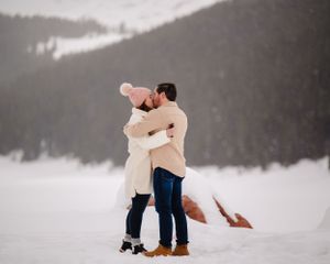 A tender embrace captured in the snow with mountains in the background.