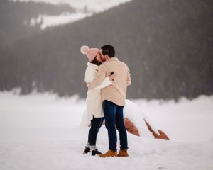 Two people share a loving embrace in cream-colored winter wear on a snowy mountain.