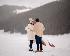 A candid winter moment captured between two people against a mountainous backdrop.