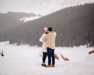 A couple in coordinating winter outfits playing in deep snow with mountain views in the background.