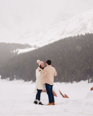 A romantic moment captured in snowy mountains as a couple kneels together in winter attire.