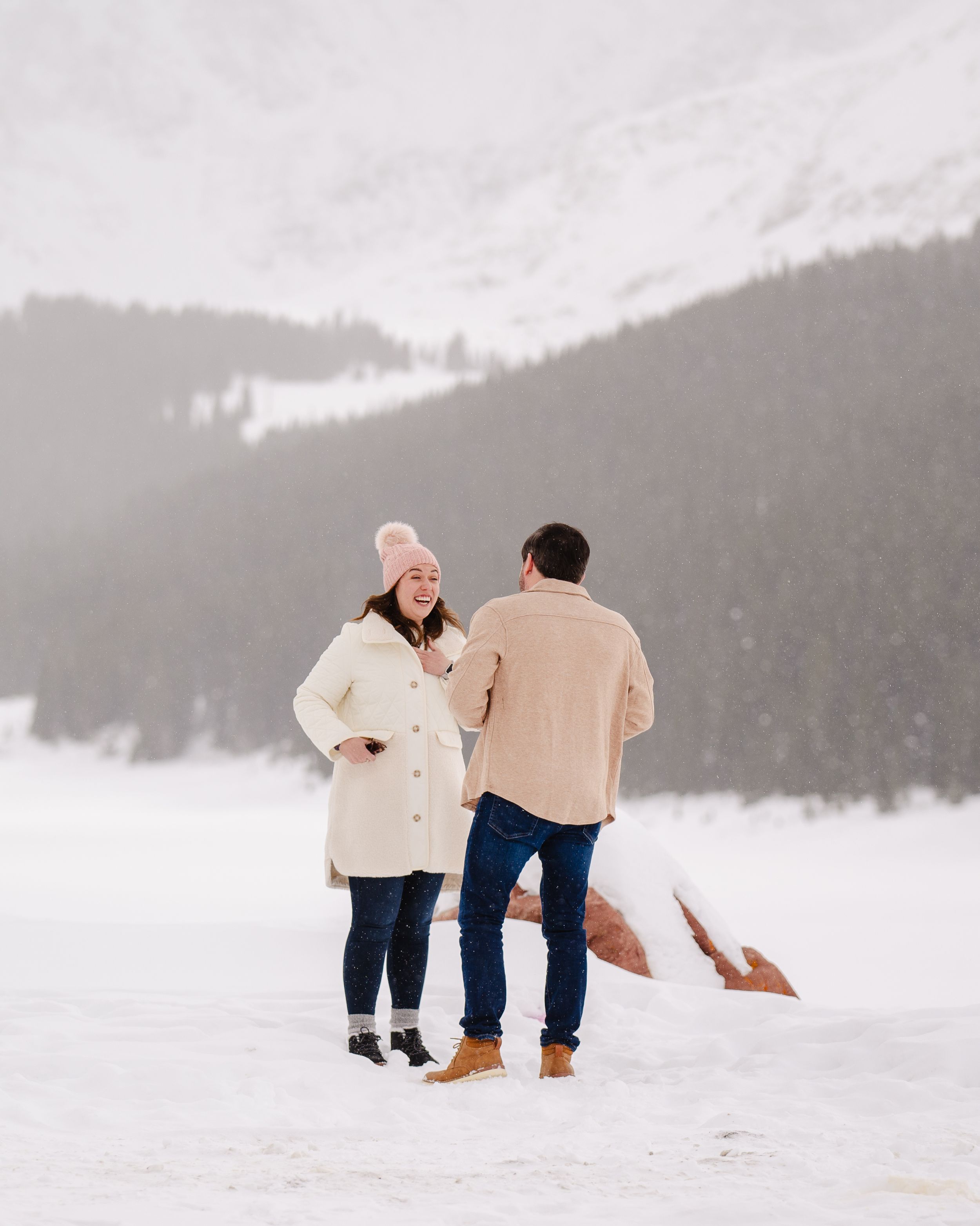 Two people share a playful moment on a snowy mountain landscape in winter attire.