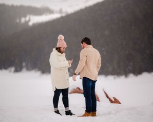 A marriage proposal scene with two people in the snow against a mountainous winter landscape.