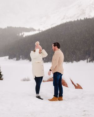 A couple celebrates their engagement in a winter wonderland setting with mountain views.