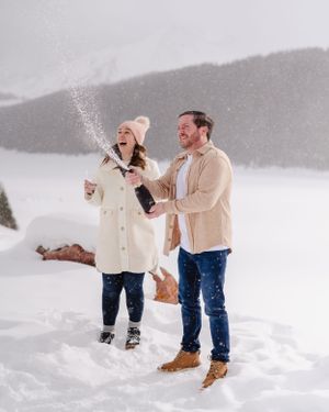 A happy couple laughs and celebrates in the snow during their winter mountain engagement.