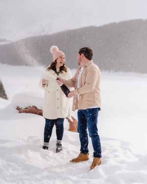 Two people share excited laughter during their snowy mountain engagement moment.