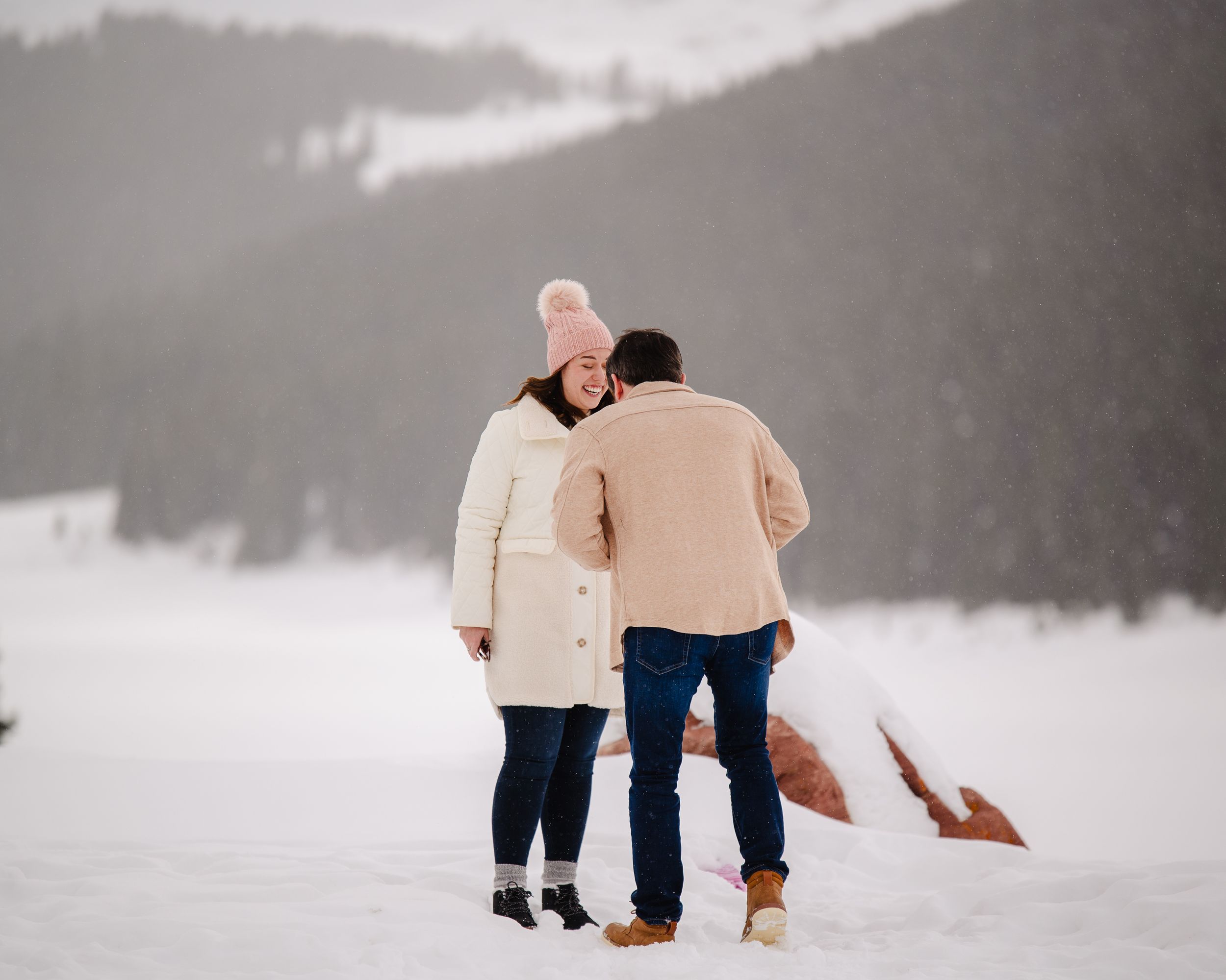 A couple embraces while standing on a snow covered mountain landscape.
