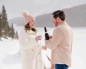 Couple sharing a celebratory moment in a snowy mountain setting with champagne bottles.