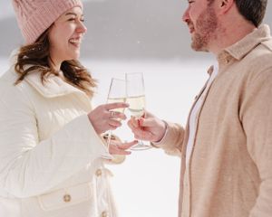 Couple clinking champagne glasses while celebrating in the snow.