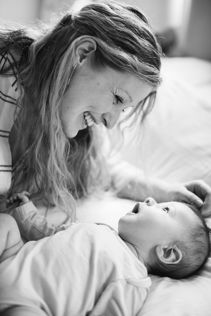 Natural newborn photography at home, featuring a mother interacting with her baby on a bed.