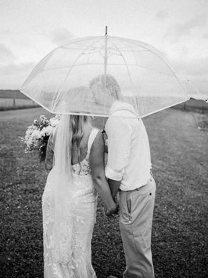 Couple sharing an intimate moment under a clear umbrella in a dreamy black and white wedding photo.
