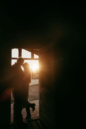 Silhouetted couple embracing in a doorway against bright sunset backlight creating a romantic mood.