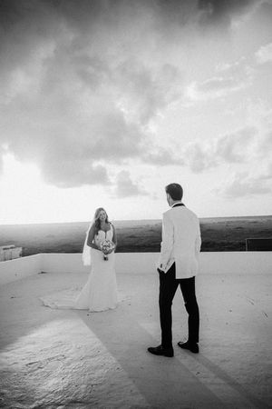 Black and white photo of a bride and groom standing on a rooftop terrace with dramatic cloudy skies.