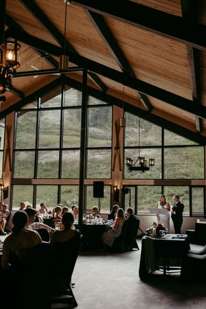 Interior view of a rustic lodge venue with exposed wooden beams and large windows overlooking a natural landscape.