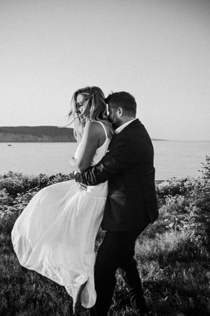 Black and white romantic wedding photograph of a couple embracing by the ocean with the bride's dress flowing in the wind.