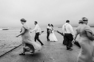Motion-blurred black and white photo of people dancing on a beach during a wedding.