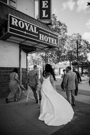 A wedding party enters the historic Royal Hotel under a black and white vintage sign on a sunny day.