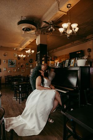 A romantic scene in a vintage bar with a white dress flowing as someone plays an upright piano under warm lighting.