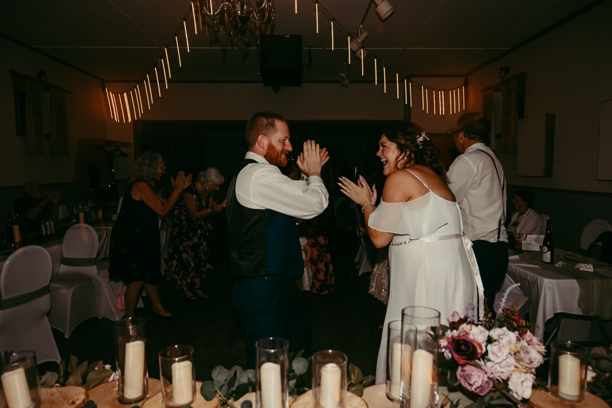 A couple shares a joyful dance at their wedding reception with candles and table settings in the foreground.