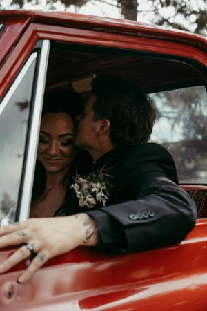 A romantic moment captured in a vintage red car with a delicate white floral corsage and moody lighting.