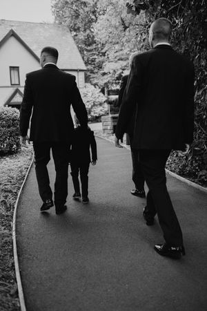 Black and white view of men in formal suits walking along a curved path by a house.