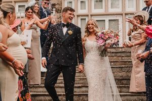 Newlywed couple descending stone steps while guests throw confetti in celebration at outdoor wedding ceremony.