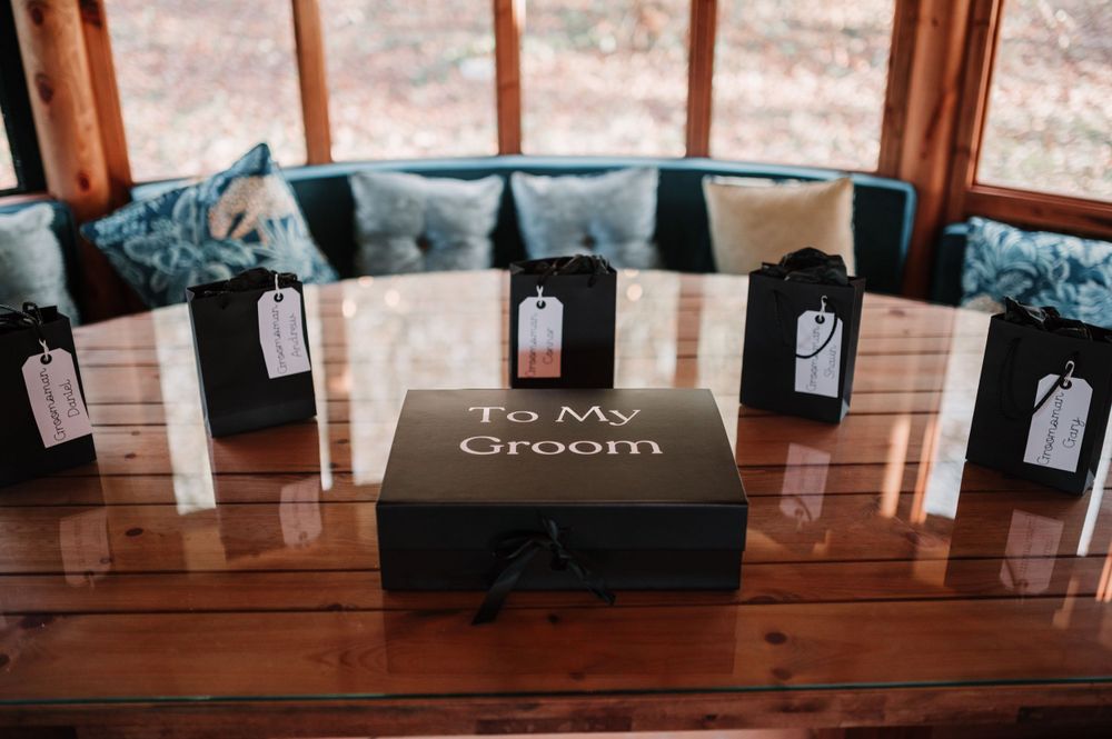Wedding favor display featuring black gift boxes and 'The Groom' box on wooden table.