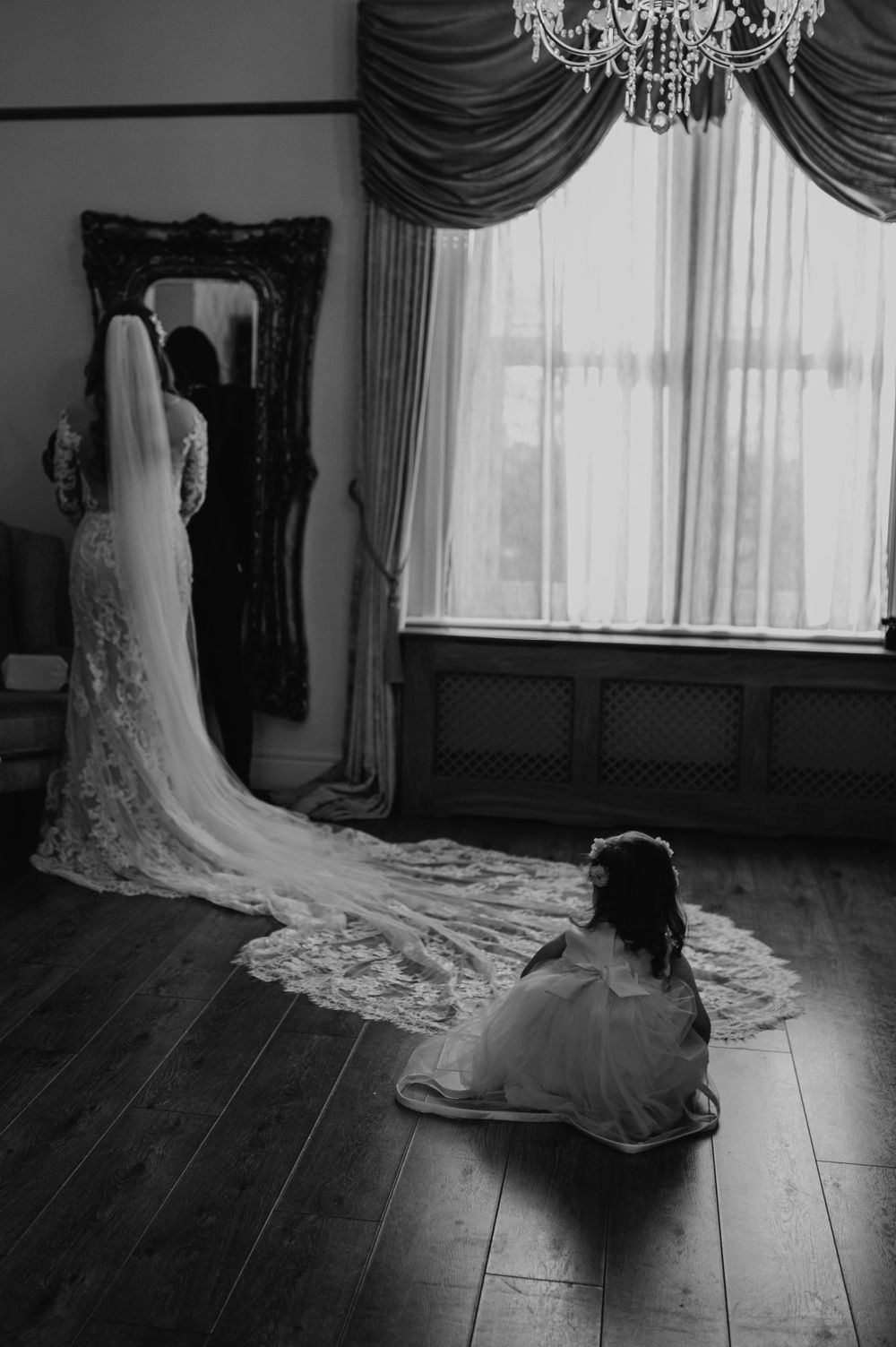 Silhouette of bride in wedding dress with flowing long veil stands before a mirror in an elegant room.