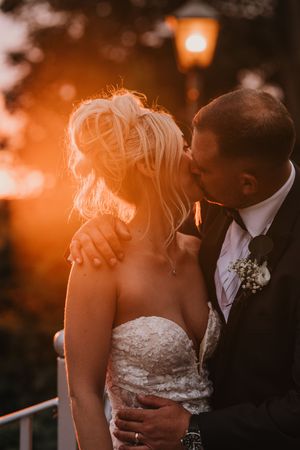 A romantic sunset wedding moment captured with a warm orange glow and vintage lamp post in the background.