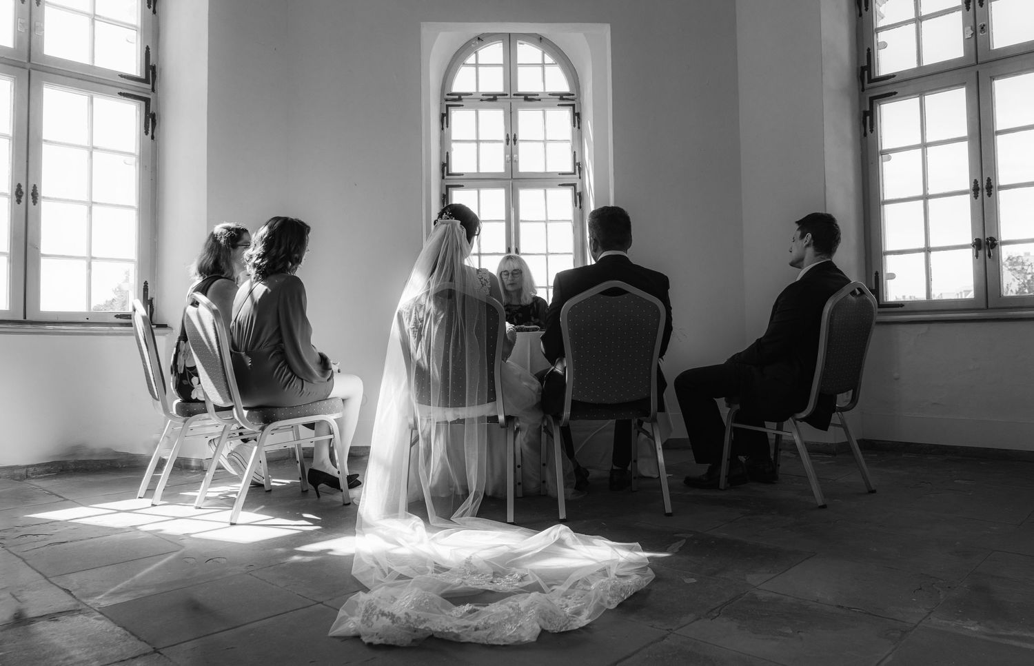 Hochzeitszene im Innenbereich mit Bräutigam, Braut, Brautjungfern und Trauzeugen, die auf Stühlen sitzen, ein formeller und eleganter Moment
