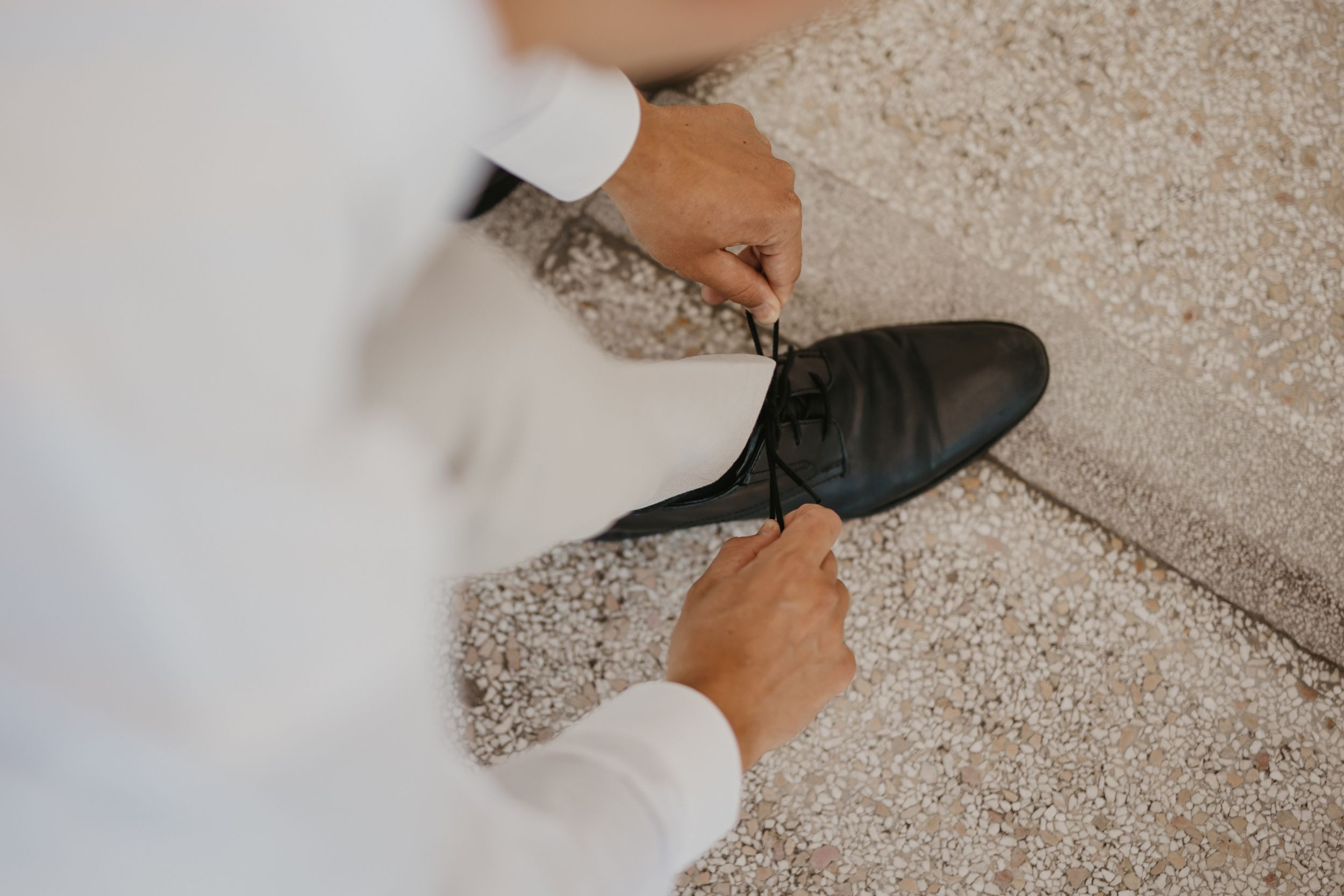 Close-up of hands tying formal black dress shoes on light carpet.