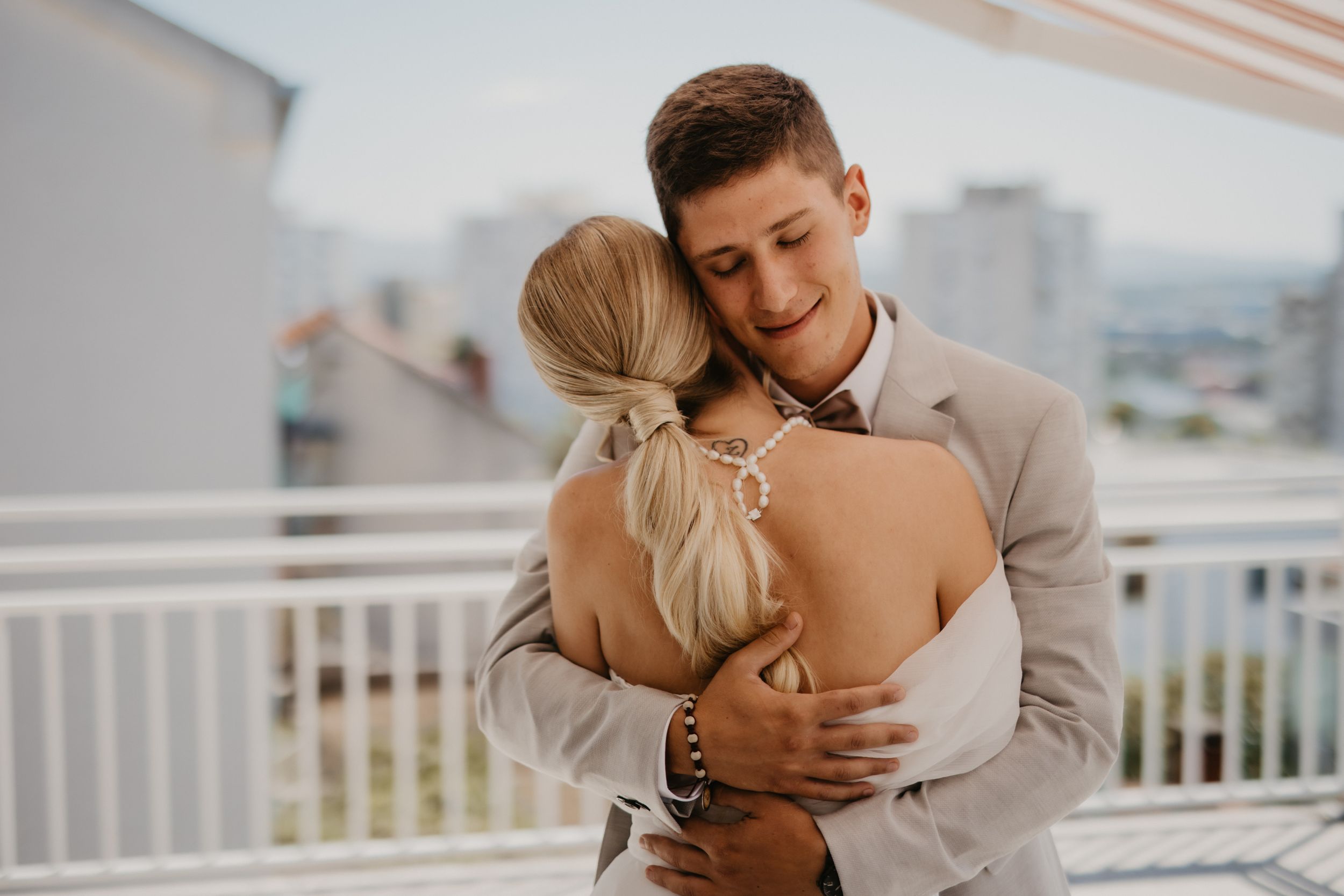 A romantic couple embraces on a sunny balcony during their wedding day.