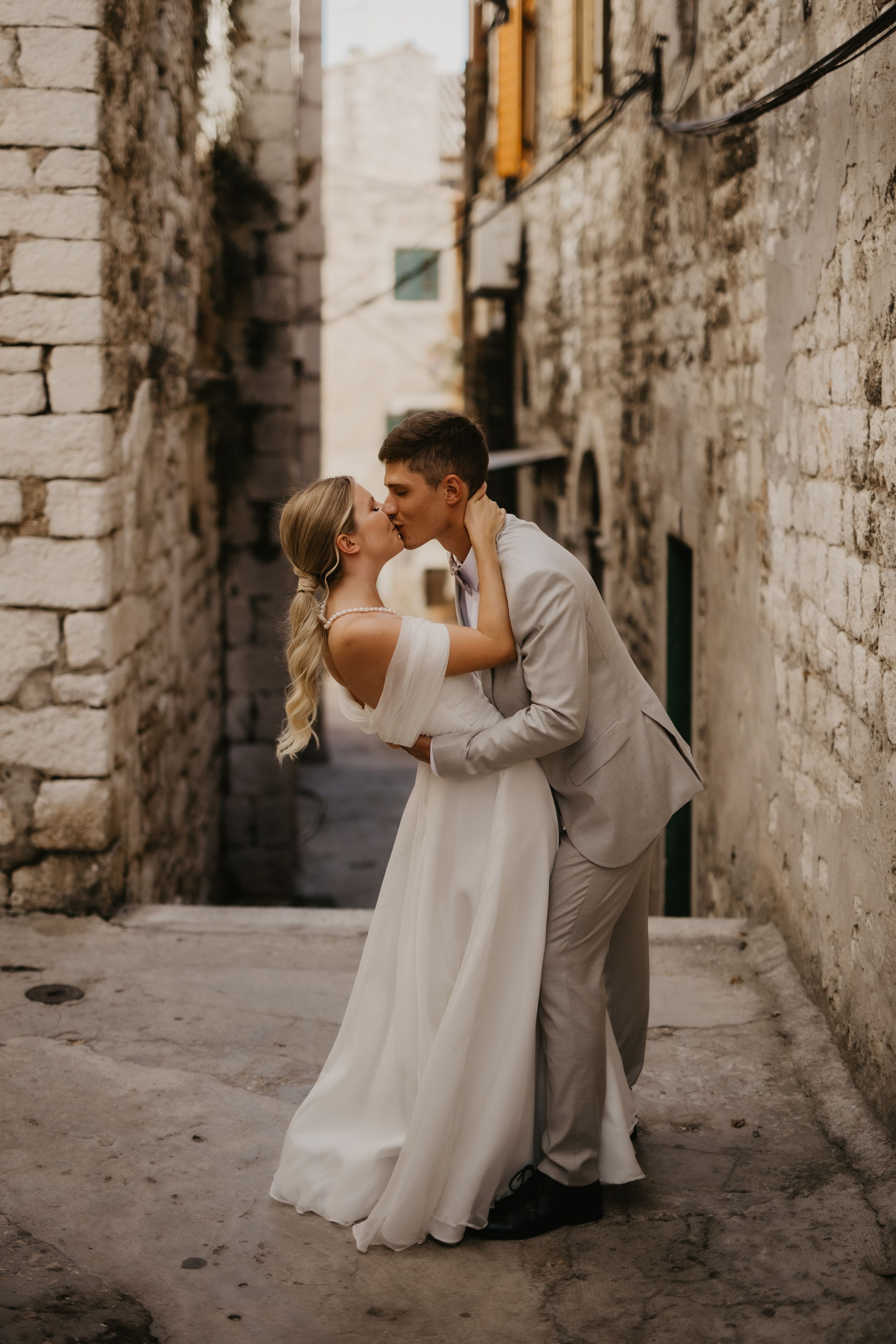 A romantic wedding couple kisses in a charming stone alleyway.