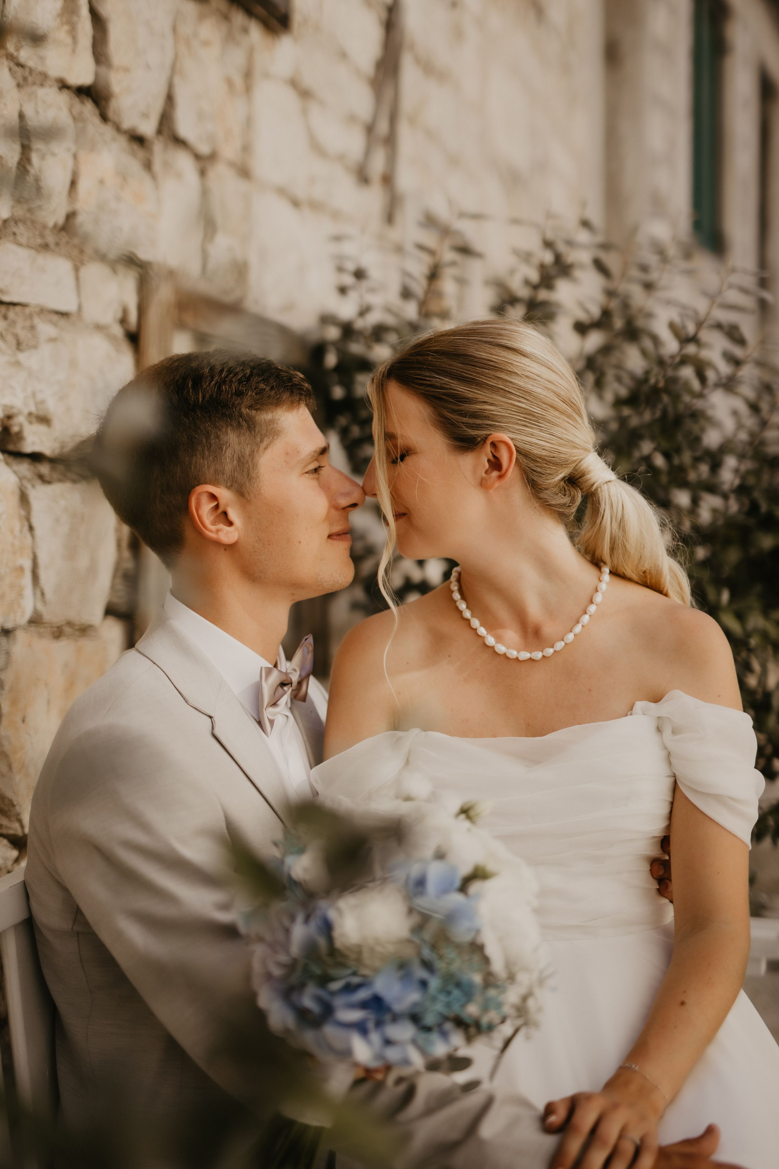 Romantic wedding portrait against stone wall with bride holding blue and white bouquet.