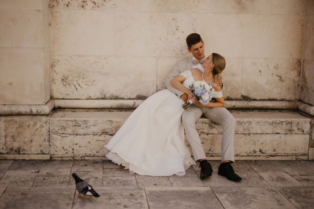 Wedding couple shares intimate moment against weathered wall with cat walking by.