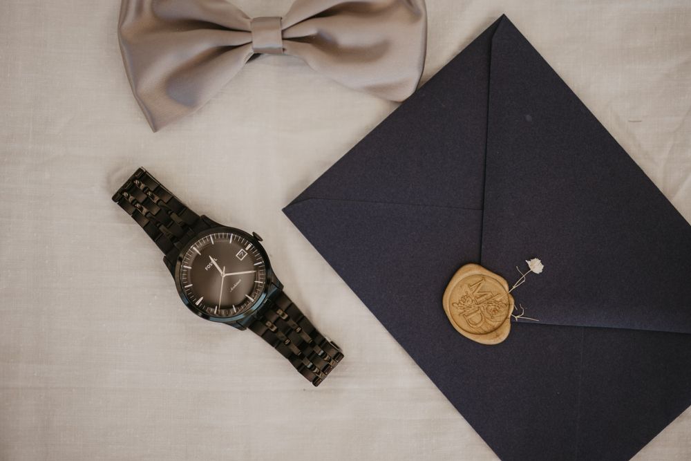 Wedding accessories including beige bowtie, watch and sealed envelope with wax stamp.