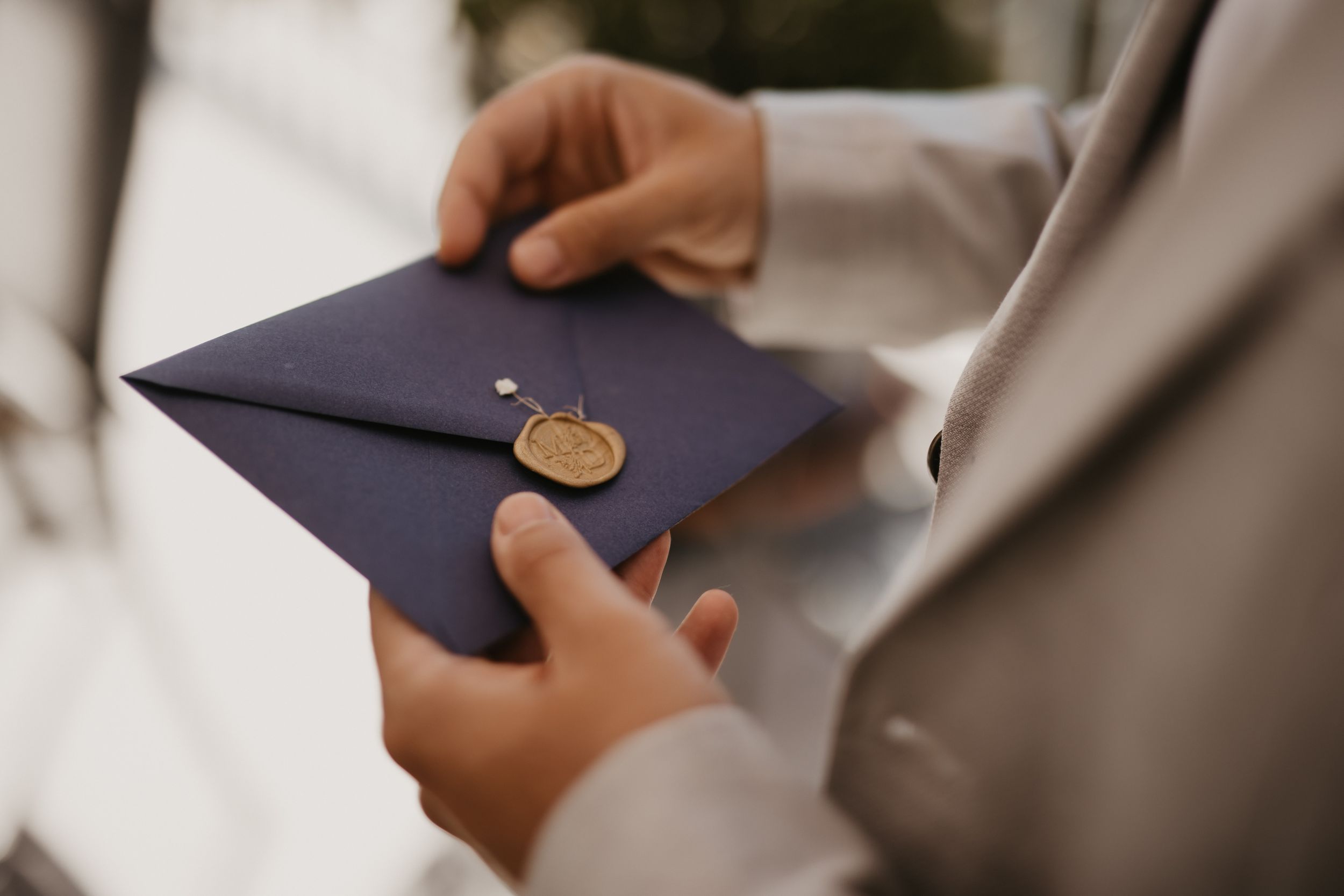 Hands holding elegant navy blue envelope sealed with gold wax stamp.