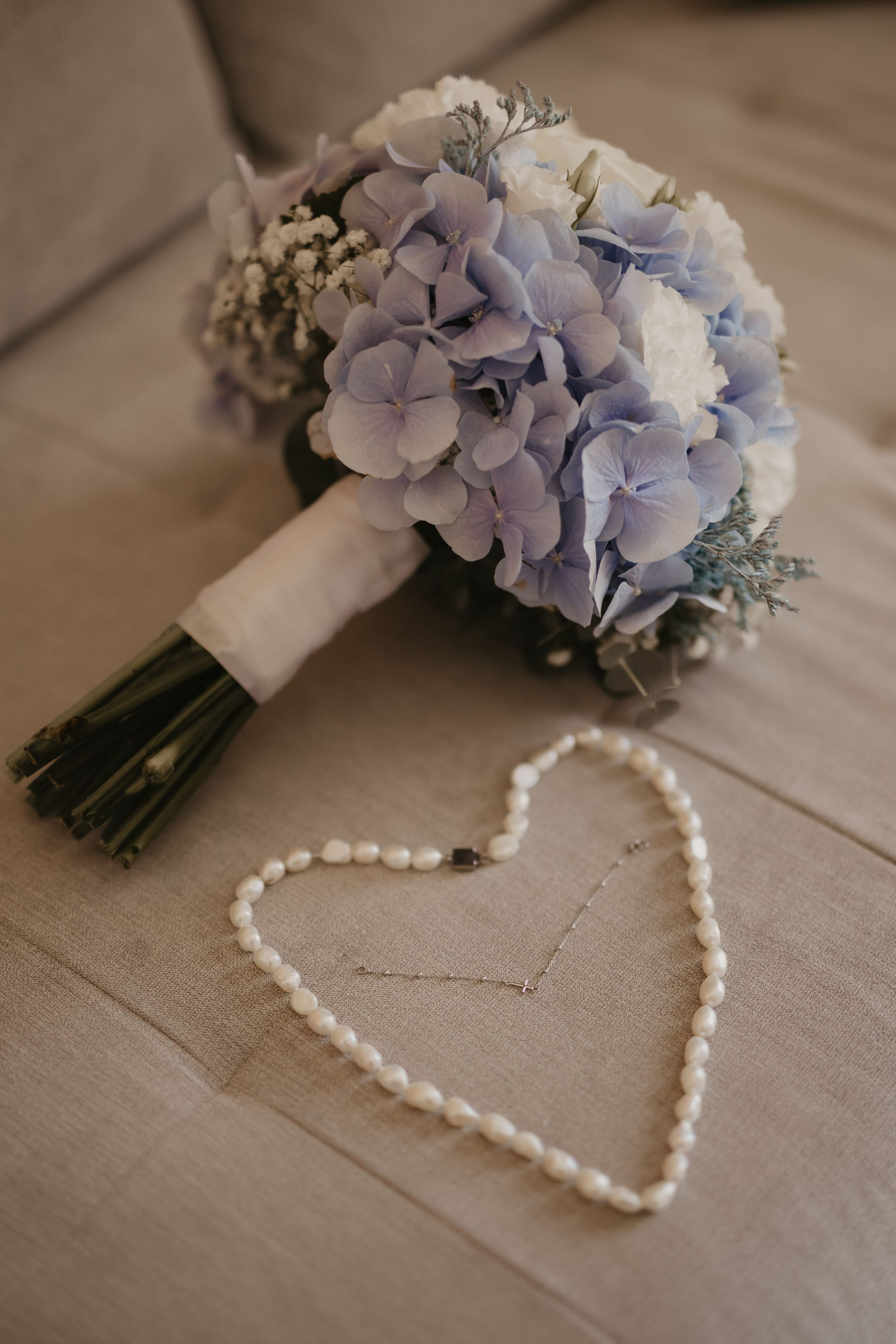 Blue and white hydrangea wedding bouquet with pearl necklace arranged in heart shape.