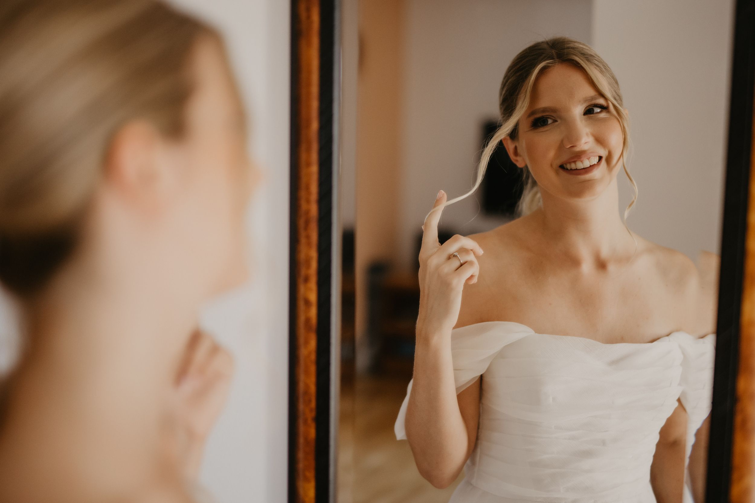 Reflection of bride in white dress looking at mirror while getting ready.