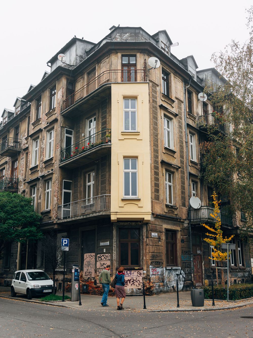 Historic yellow corner apartment building with ornate balconies and graffiti-covered ground floor in an urban setting.