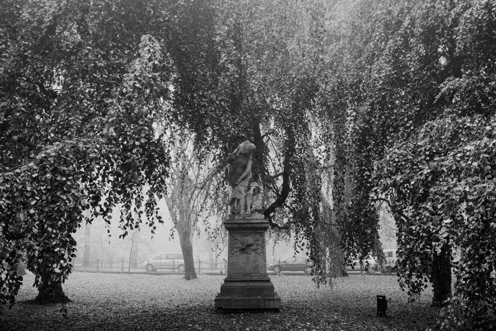 Misty garden scene with weeping willow trees and stone monuments in soft natural light.