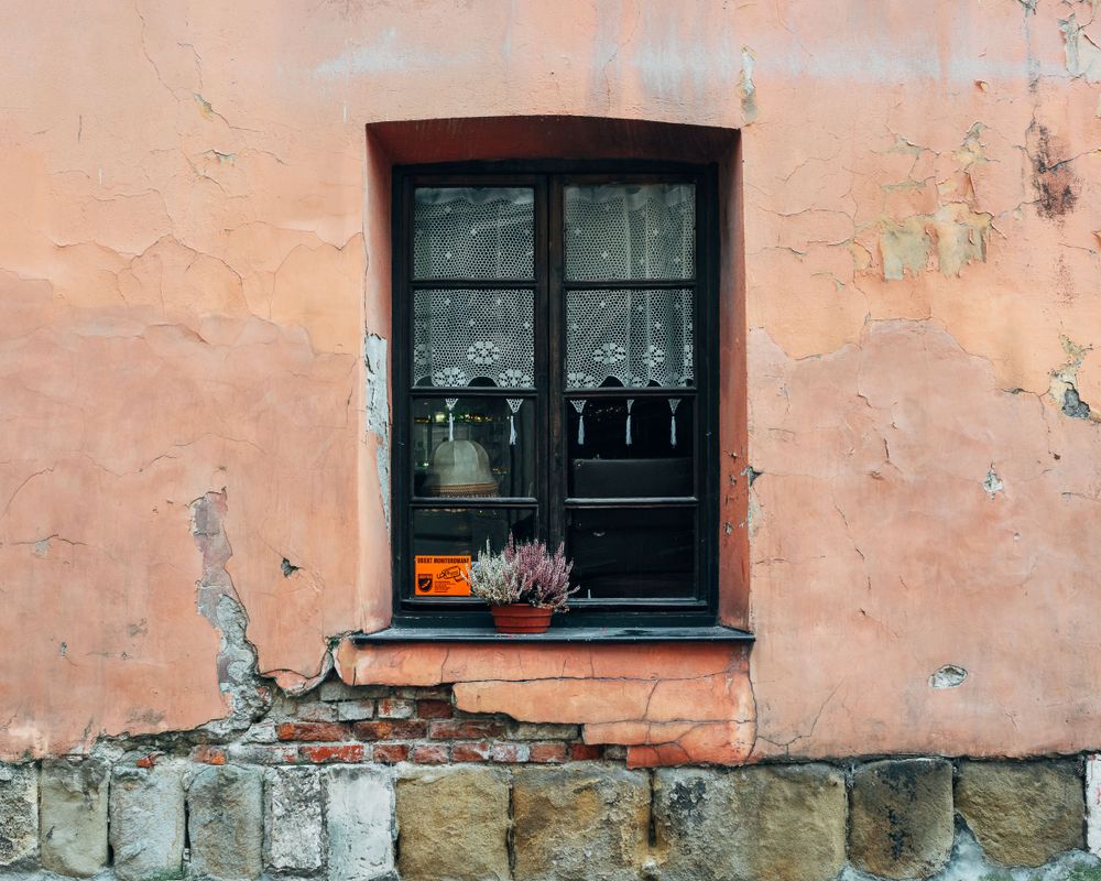 Weathered pink wall with black-framed window and peeling paint texture.