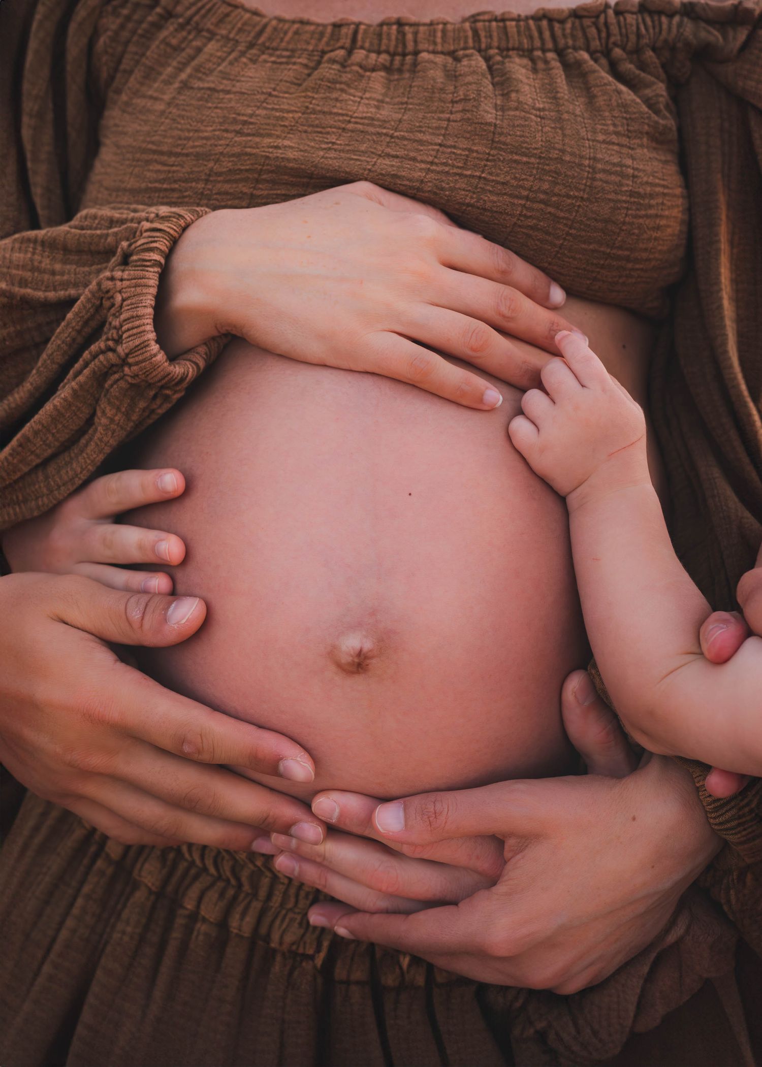 Gentle hands cradling a pregnant belly in brown fabric, showing tender moments of anticipation.