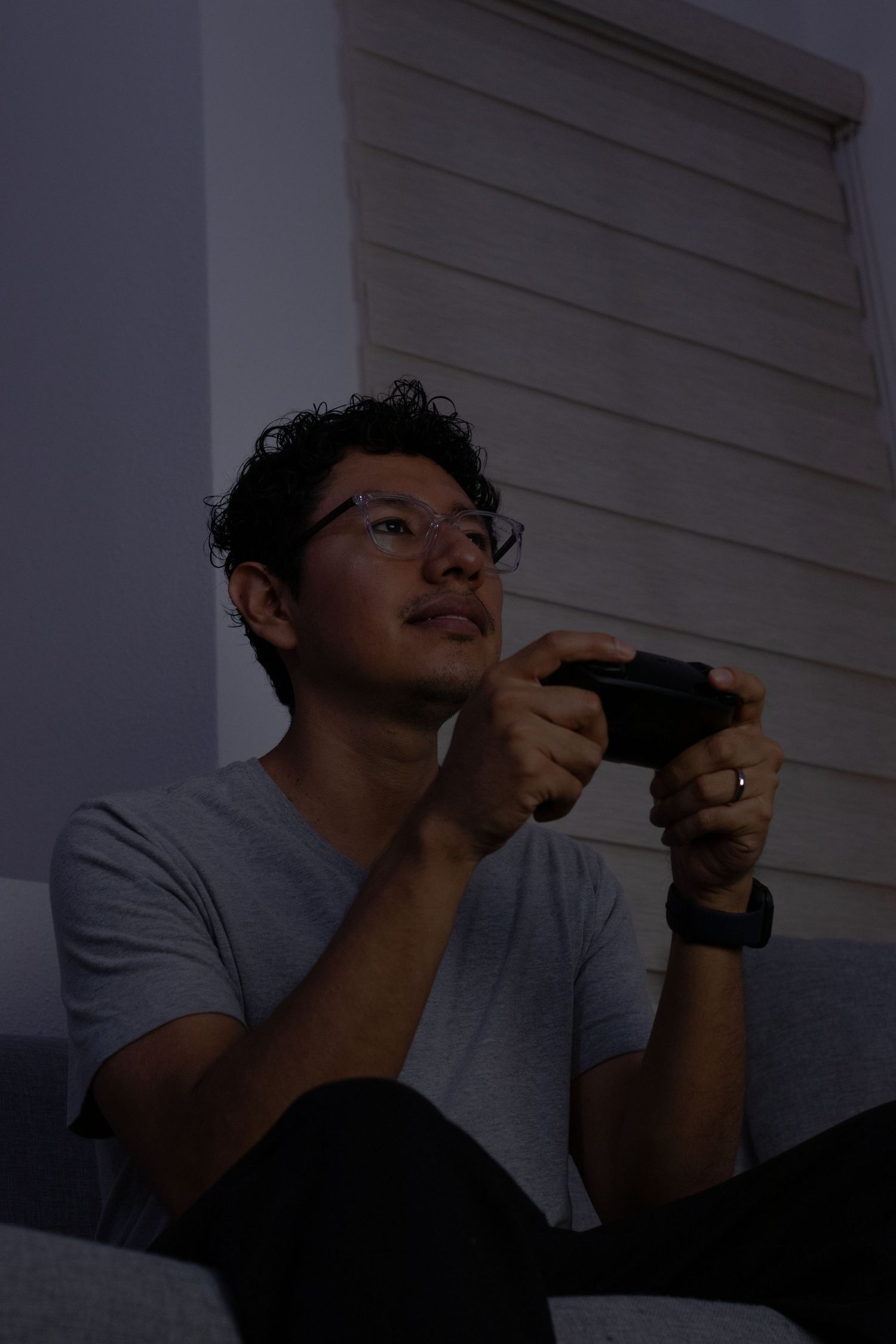 A person plays a handheld video game console while wearing a gray t-shirt in low light conditions.