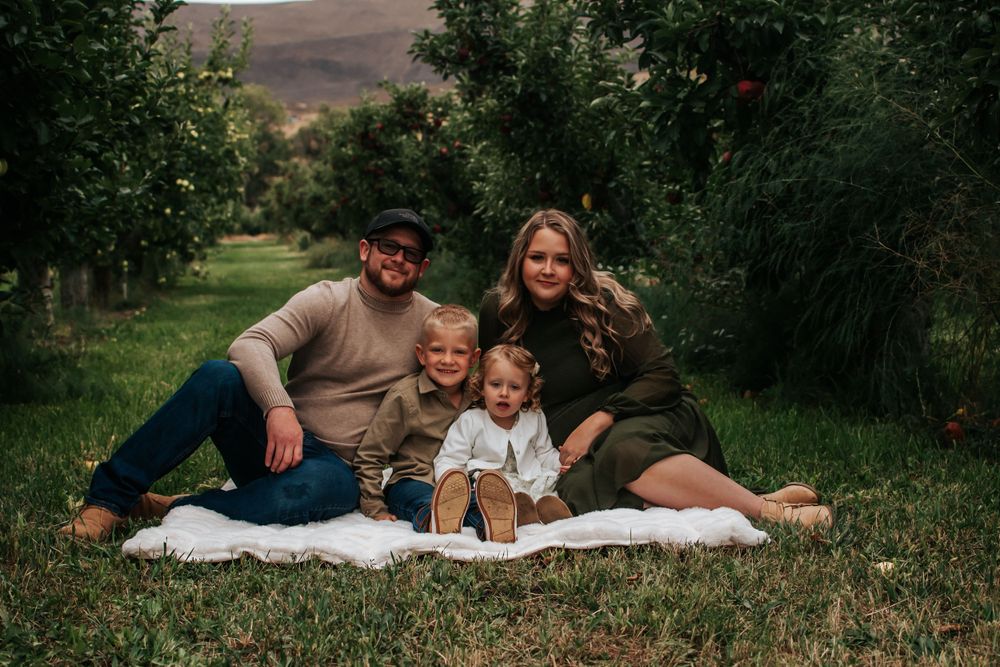 A family sits together on a blanket in an orchard during a photo session in Tri Cities, Washington.