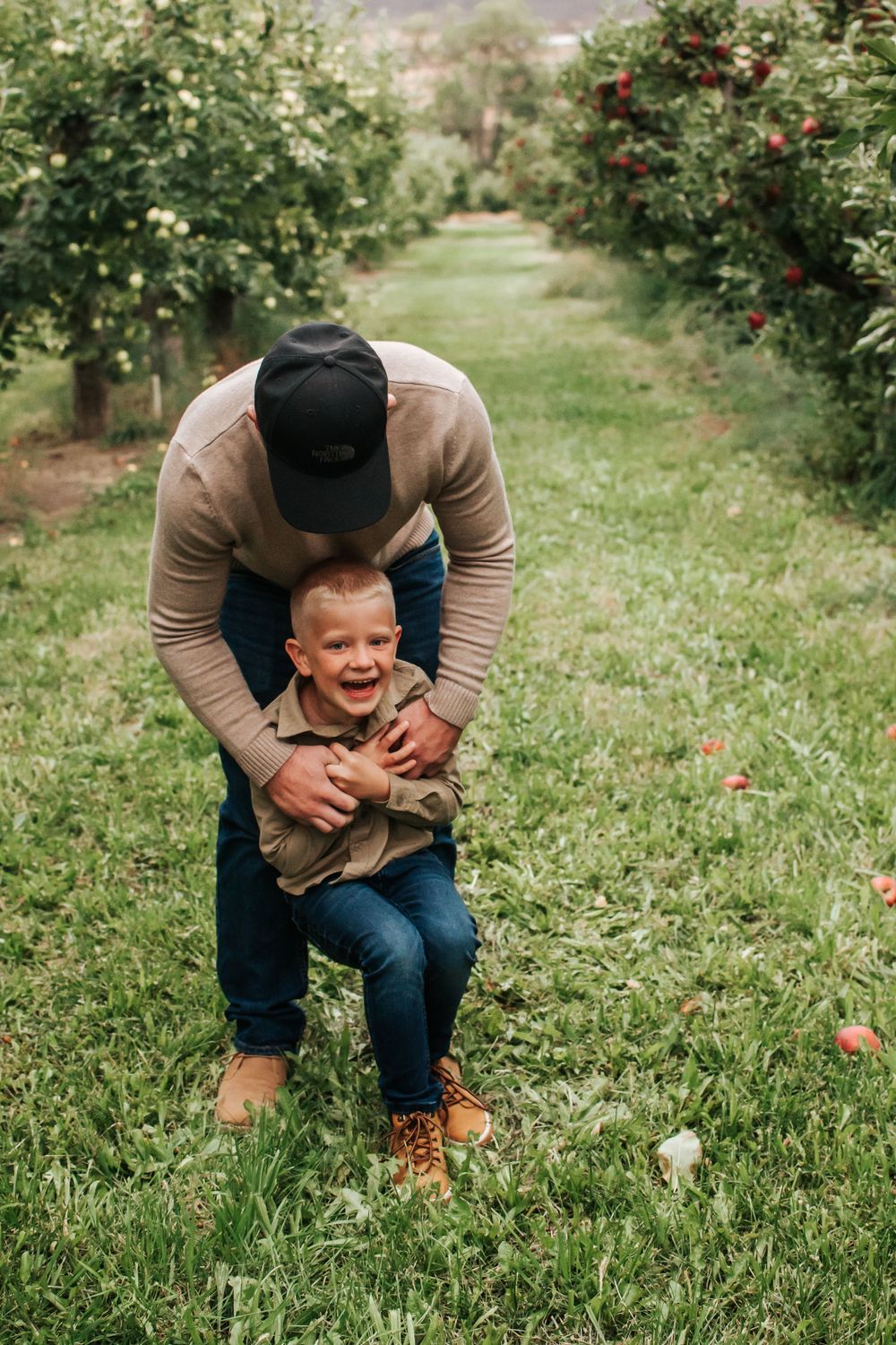 A playful moment between father and son in an apple orchard on a sunny day in Benton City, Washington.