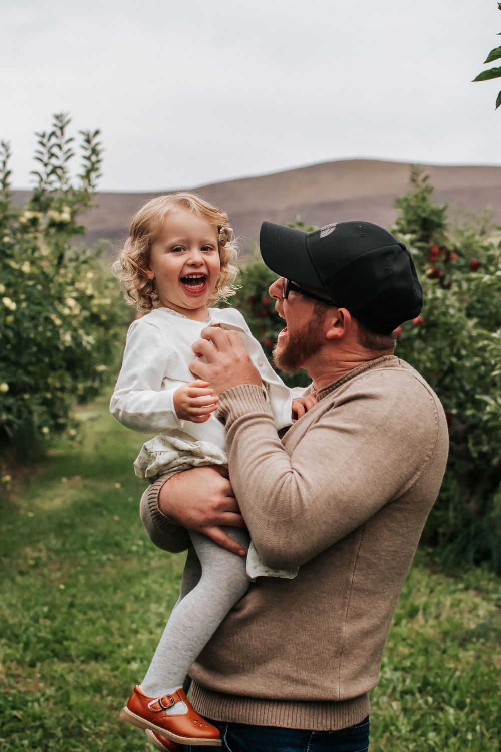 A heartwarming moment of play and laughter in an apple orchard on an overcast day in Benton City, Washington.