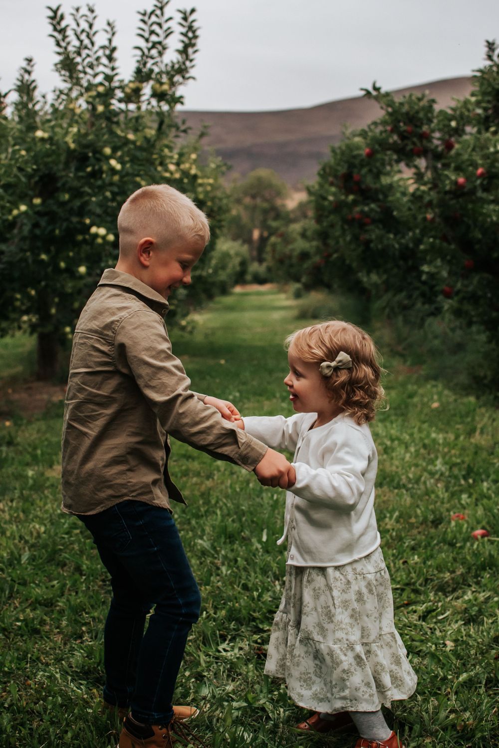 Two children playing and dancing together between rows of apple trees in an orchard in Tri Cities, Washington.