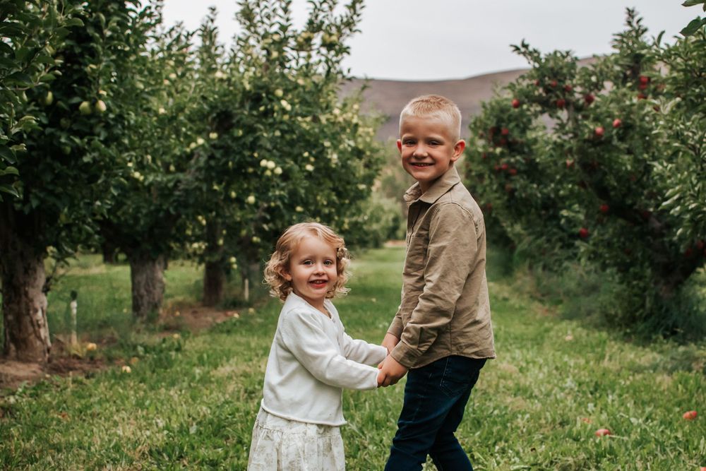 Children holding hands and playing together in a scenic orchard with rolling hills in the background in Benton City, Washington.