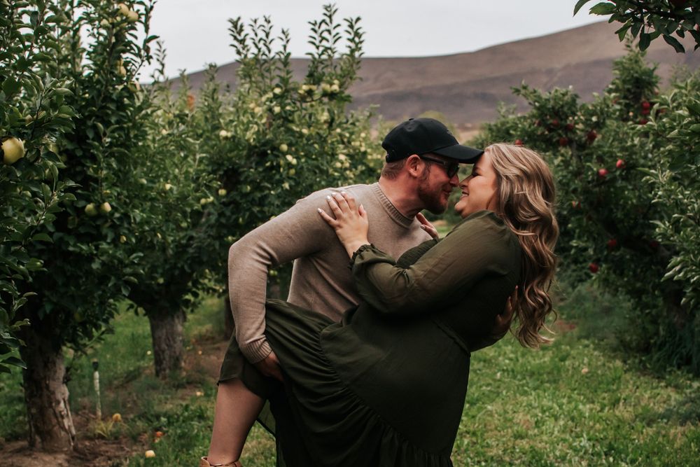 Romantic couple embracing among apple trees in an apple orchard at sunset in Benton City, Washington.